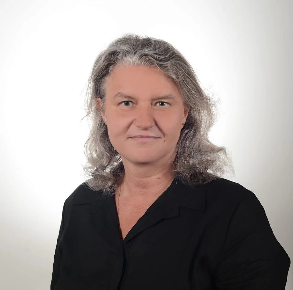 Portret studyjny pani Iwony Brylok. Kobieta jest w średnim wieku i jest ubrana w czarną koszulę z kołnierzykiem.